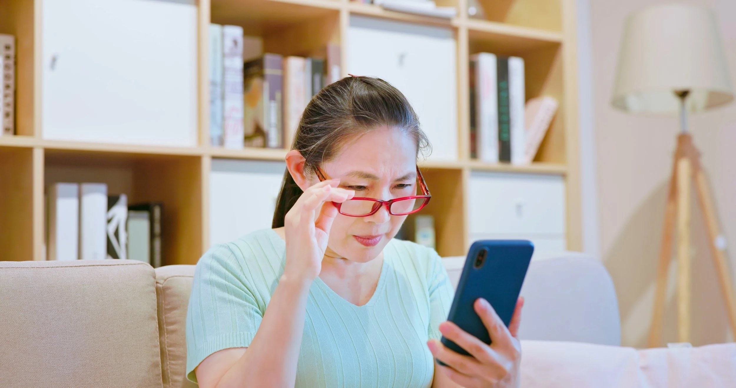 A woman with red glasses looks at her smartphone realizing that her fatigue might have been caused by a vitamin D efficiency.